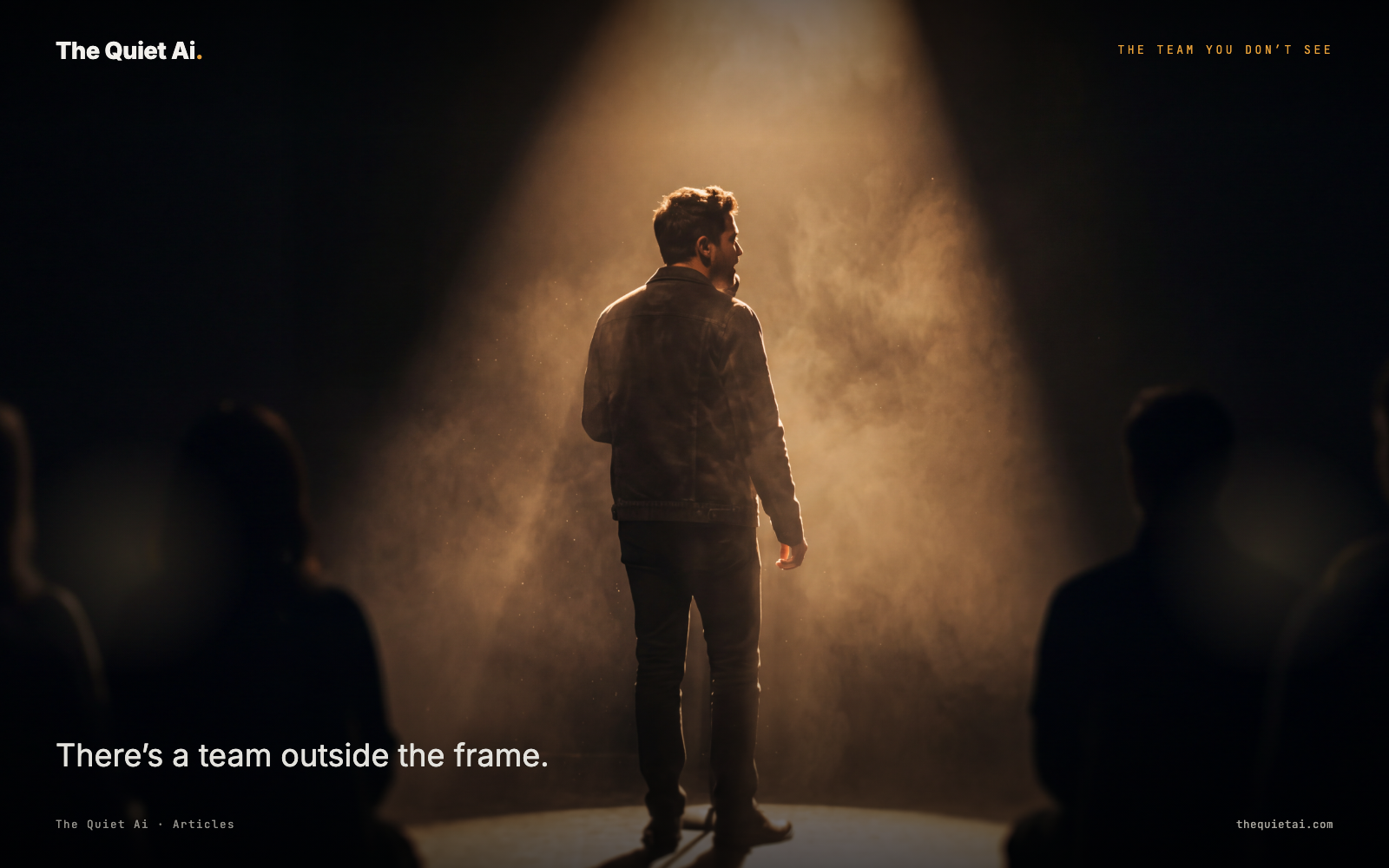 A single figure standing in a spotlight on a stage, silhouettes of a larger group visible just outside the light.
